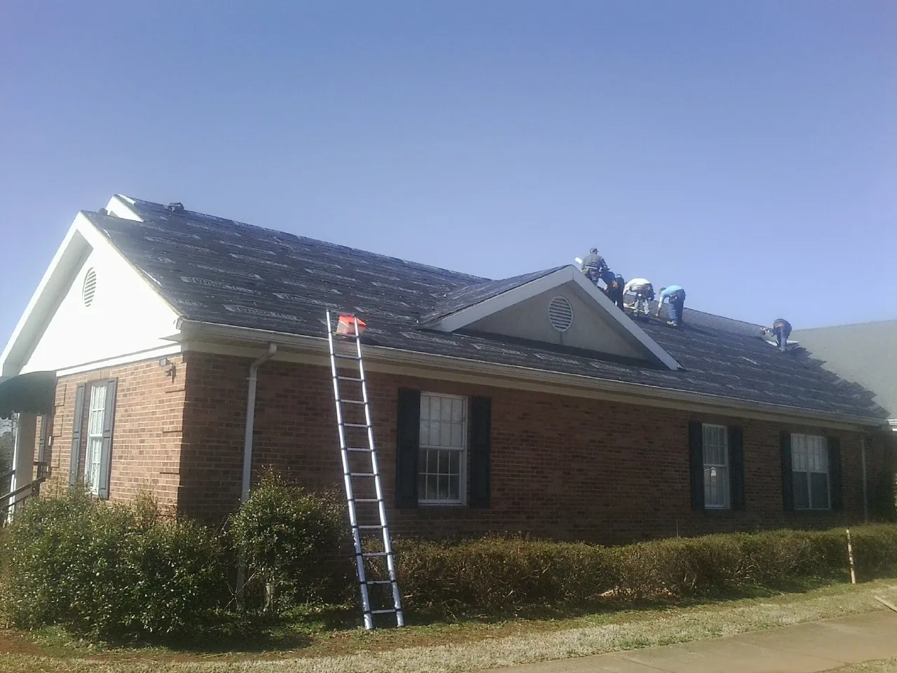 Crew tearing shingles off a brick ranch roof with a ladder set — Emergency Roof Repair work by our crew in Kinderhook