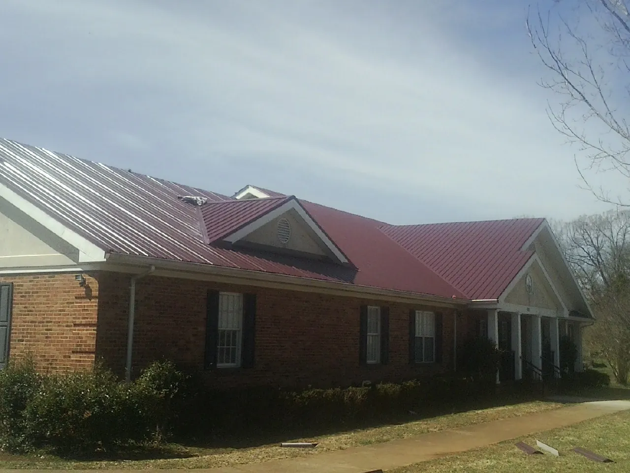 Red metal roof with gabled entries on a long brick building, from a Hail Damage Roof Repair job in Kinderhook