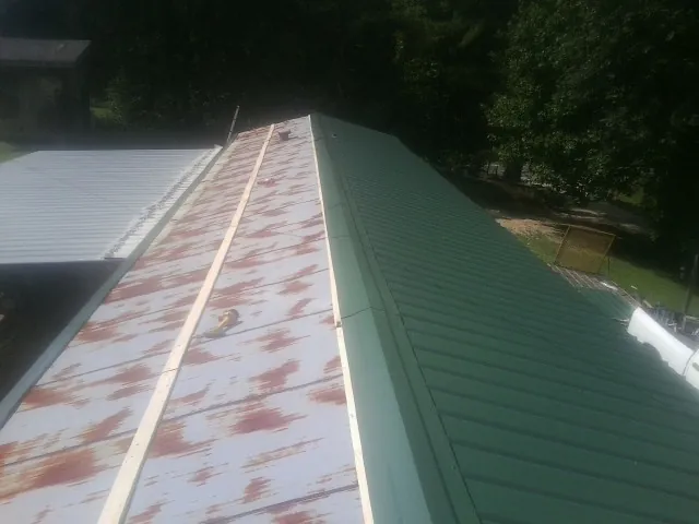 Old rusted panels beside newly installed green metal roofing — Wind Damage Roof Repair by Roofing Brothers in Kinderhook