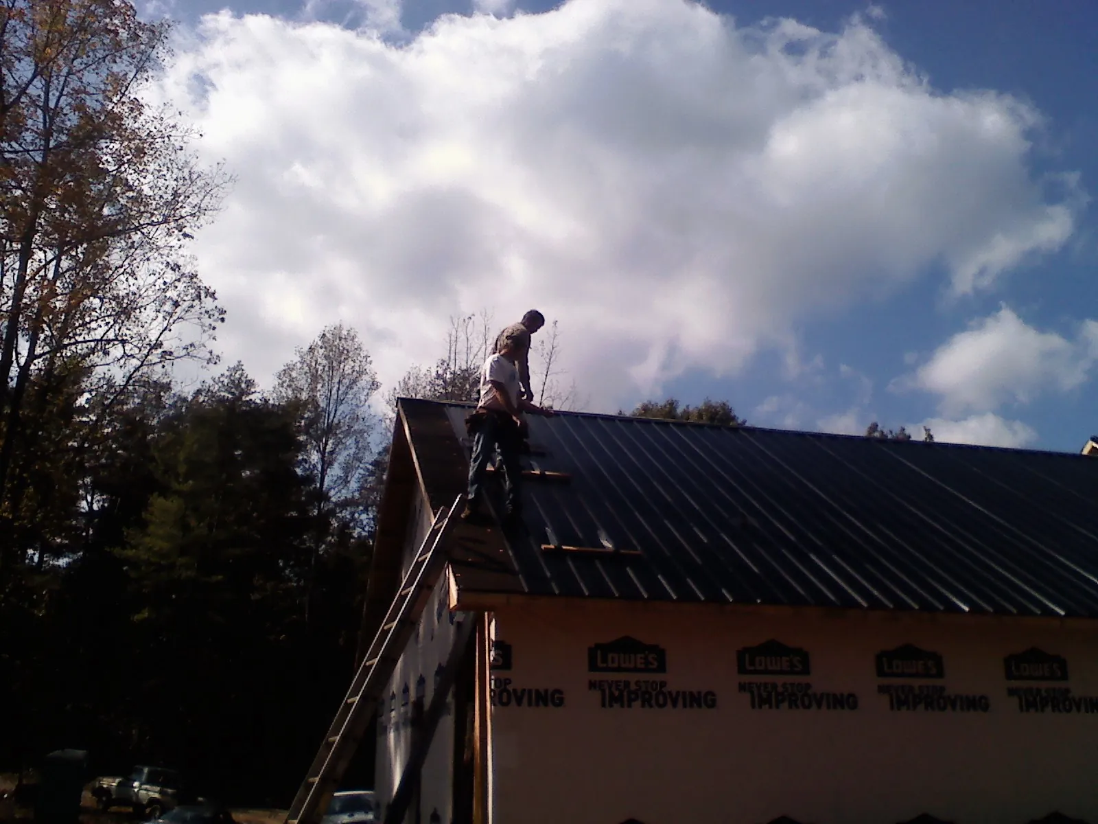Roofer fastening dark metal panels high against a cloudy sky, from a Roof Inspection job in Kinderhook