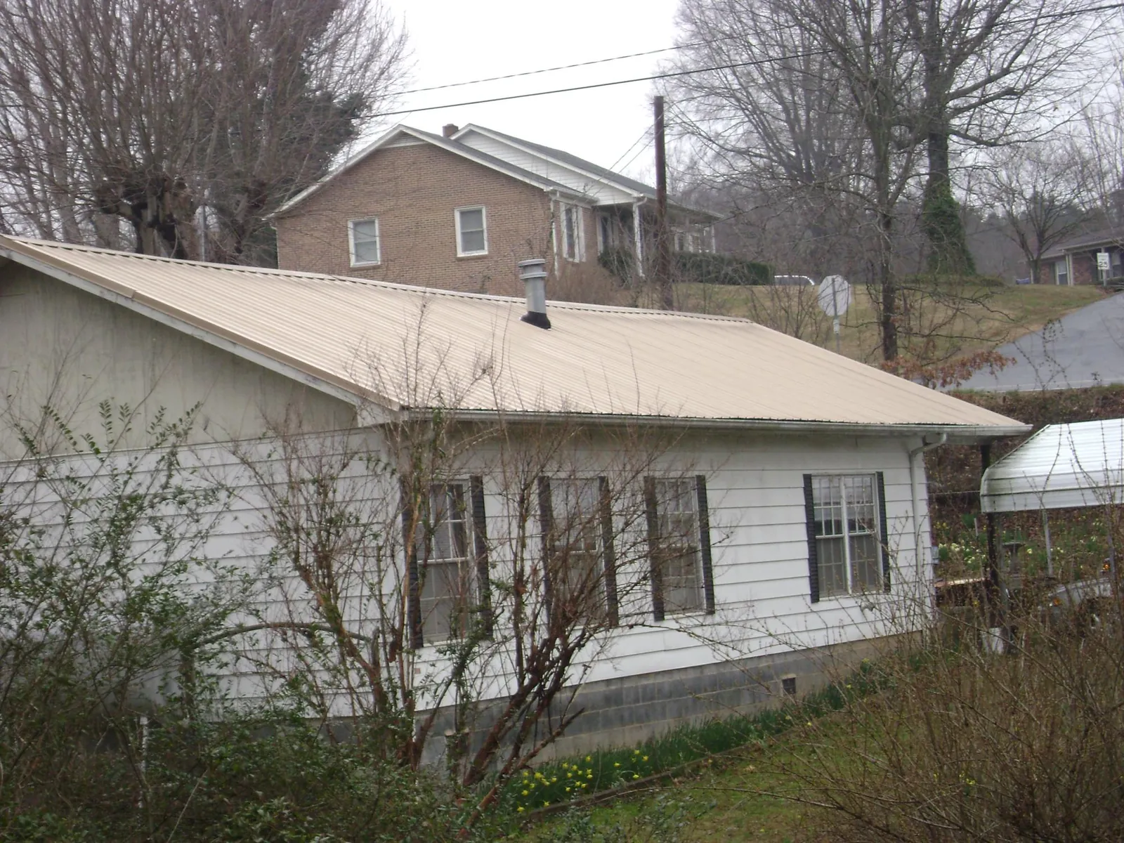 Tan metal roof on a white sided house set into a hillside — Commercial Roofing by Roofing Brothers in Kinderhook